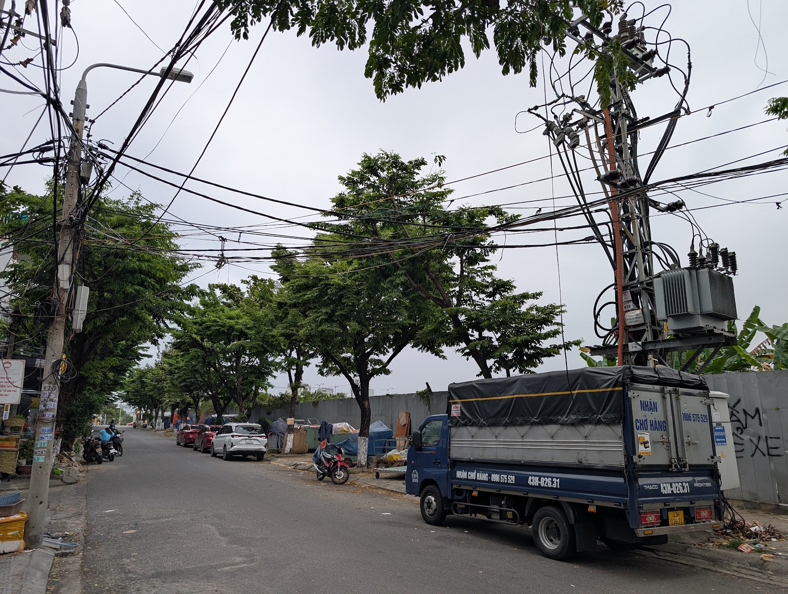 Photo of two utility poles on wither side of a street with some medium
                 sized trees lining the street and a box truck on one side. On the same
                 side, no buildings are on the block so the cables show up nicely
                 against the sky.