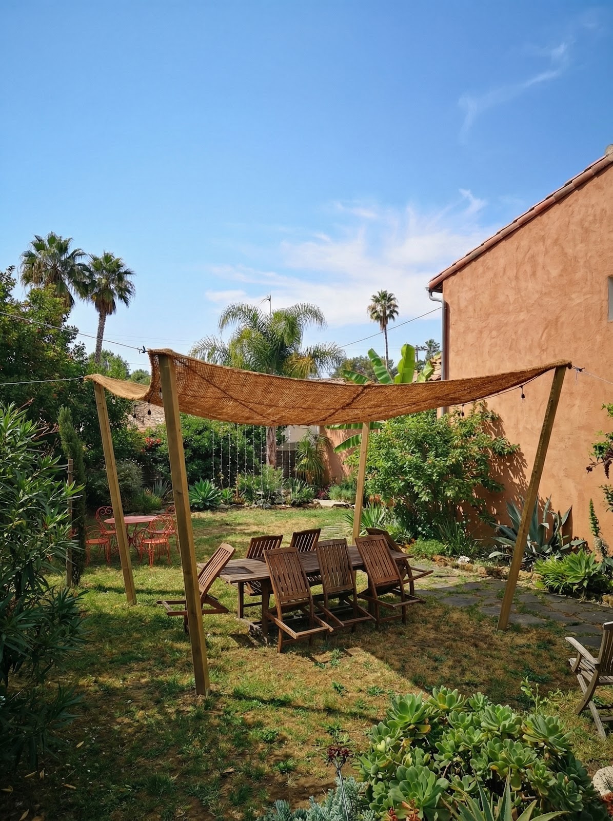 Coir shade sail mounted on wood posts over garden dining table