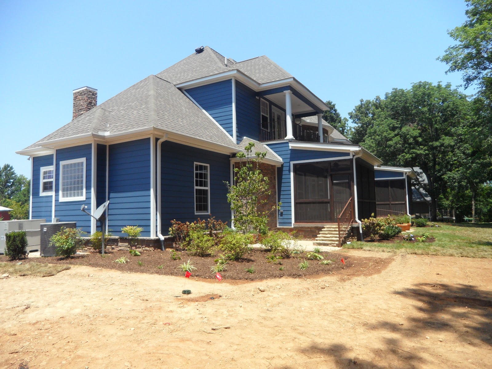 Rear exterior of a blue two-story residential building with a grey shingle roof, stone chimney, and screened-in porch in East Tennessee.