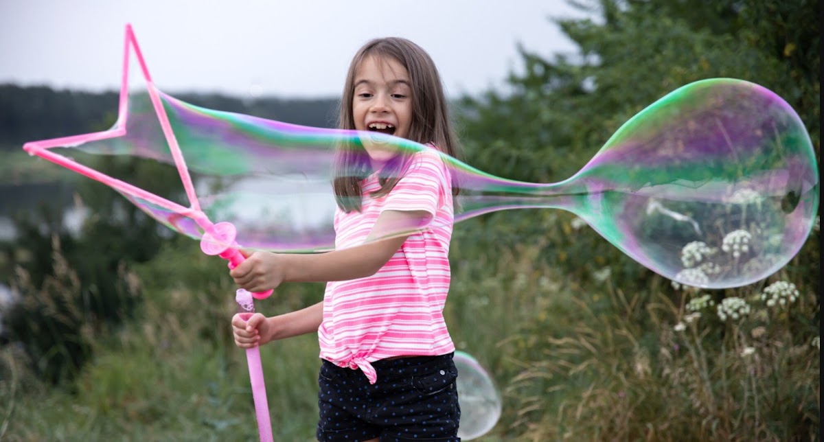 Girl making giant soap bubble in field