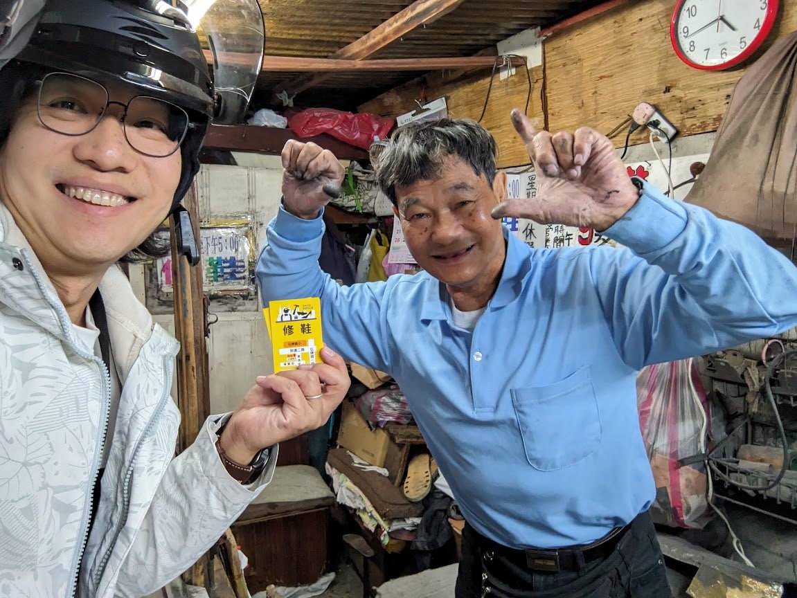 手持修鞋名片，賴師傅笑容洋溢比出手勢