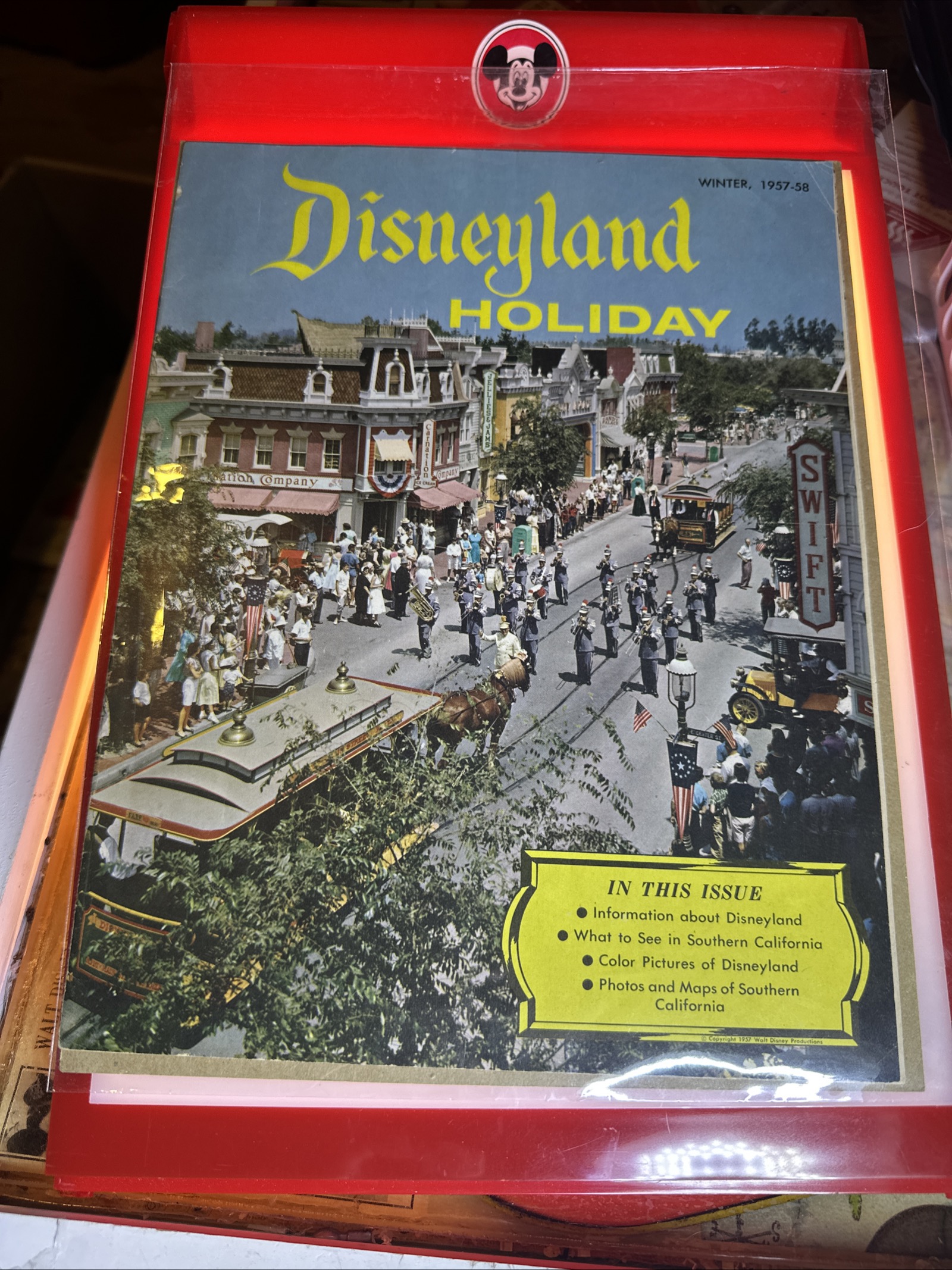 Disneyland Holiday Magazine Winter 1957–58 souvenir guidebook, 8.5 by 11 inches, showing Main Street USA parade cover, housed in red plastic protector with Mickey Mouse sticker