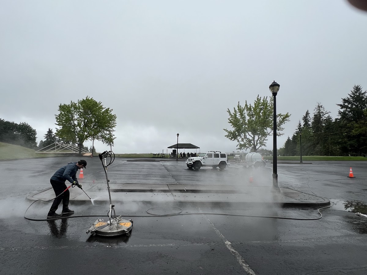 Rinse It Off crew cleaning a commercial parking lot with surface cleaner and hot water rig