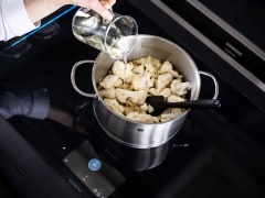 Ngắt nhỏ bông cải và rửa sạch với nước muối nhiều lần. Để ráo bông cải rồi thái nhỏ. Lột vỏ 2 tép tỏi và hành tây rồi băm nhỏ. Bắc một cái nồi lên bếp, rót dầu ăn vào đun nóng, phi thơm hành tây và tỏi rồi cho bông cải trắng vào xào 5 phút. Rót rượu trắng vào rồi nấu sôi hỗn hợp vài phút.