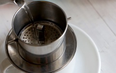 Cho vào phin 2 muỗng cà phê, dùng gạt ép cà phê vừa phải, không quá chặt cũng không quá lỏng. Đầu tiên bạn rót vào 20ml nước sôi, để khoảng 15 giây cho cà phê ngấm rồi tiếp tục cho 60ml nước sôi còn lại. Đậy nắp phin và chờ cà phê rơi xuống đến khi hết nước.