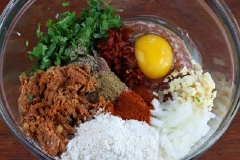 Cho tất cả nguyên liệu làm thịt viên: Thịt bò xay, 1 quả trứng, 1/2 củ hành tây băm nhỏ, 1/2 số tỏi băm, 1/2 số ngò rí, muối, ớt bột, 1/2 số bột thì là vào một tô lớn. Trộn đều tất cả lại với nhau.