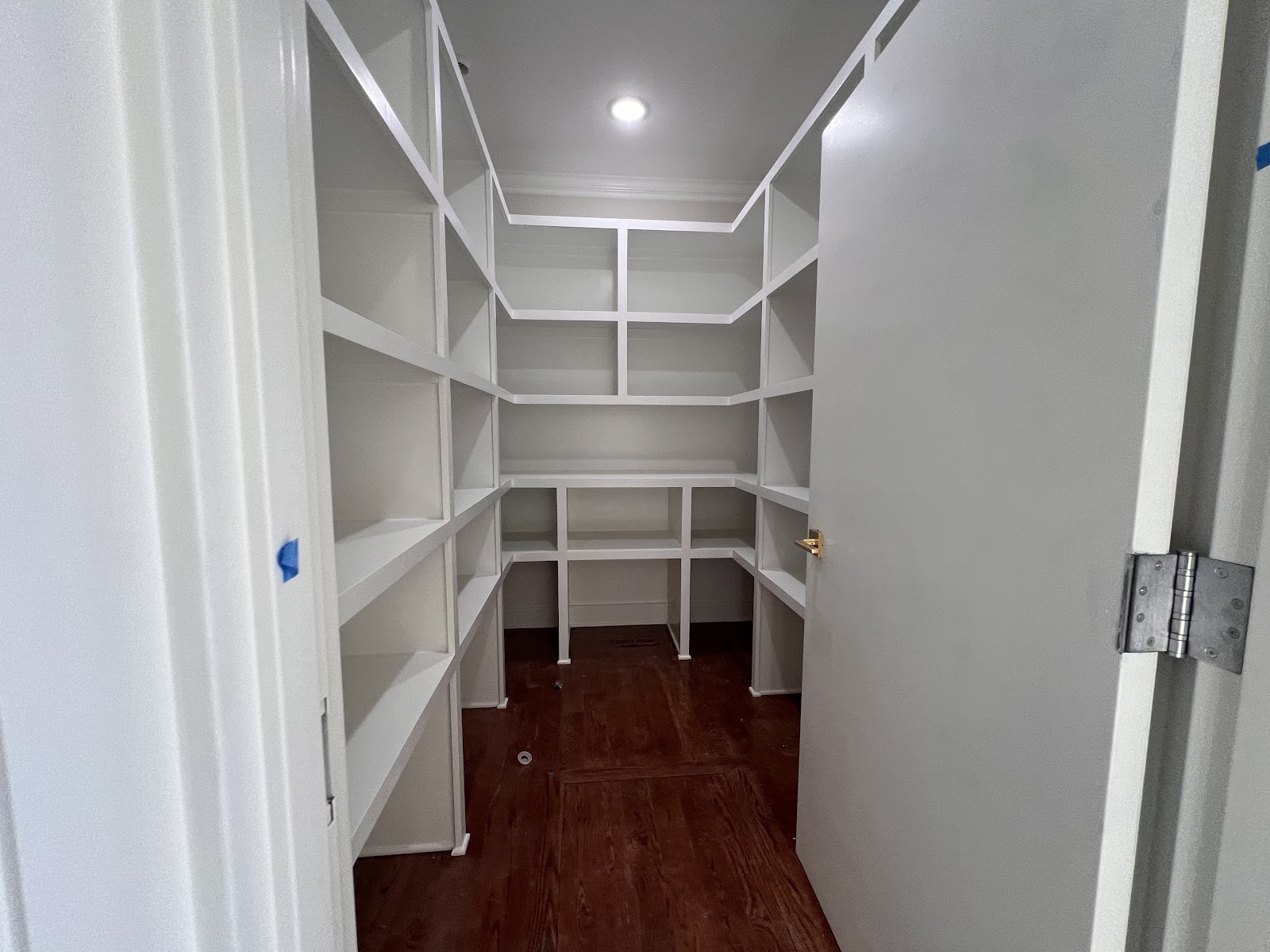 Interior view of a finished residential storage area with white built-in shelving and wood flooring.