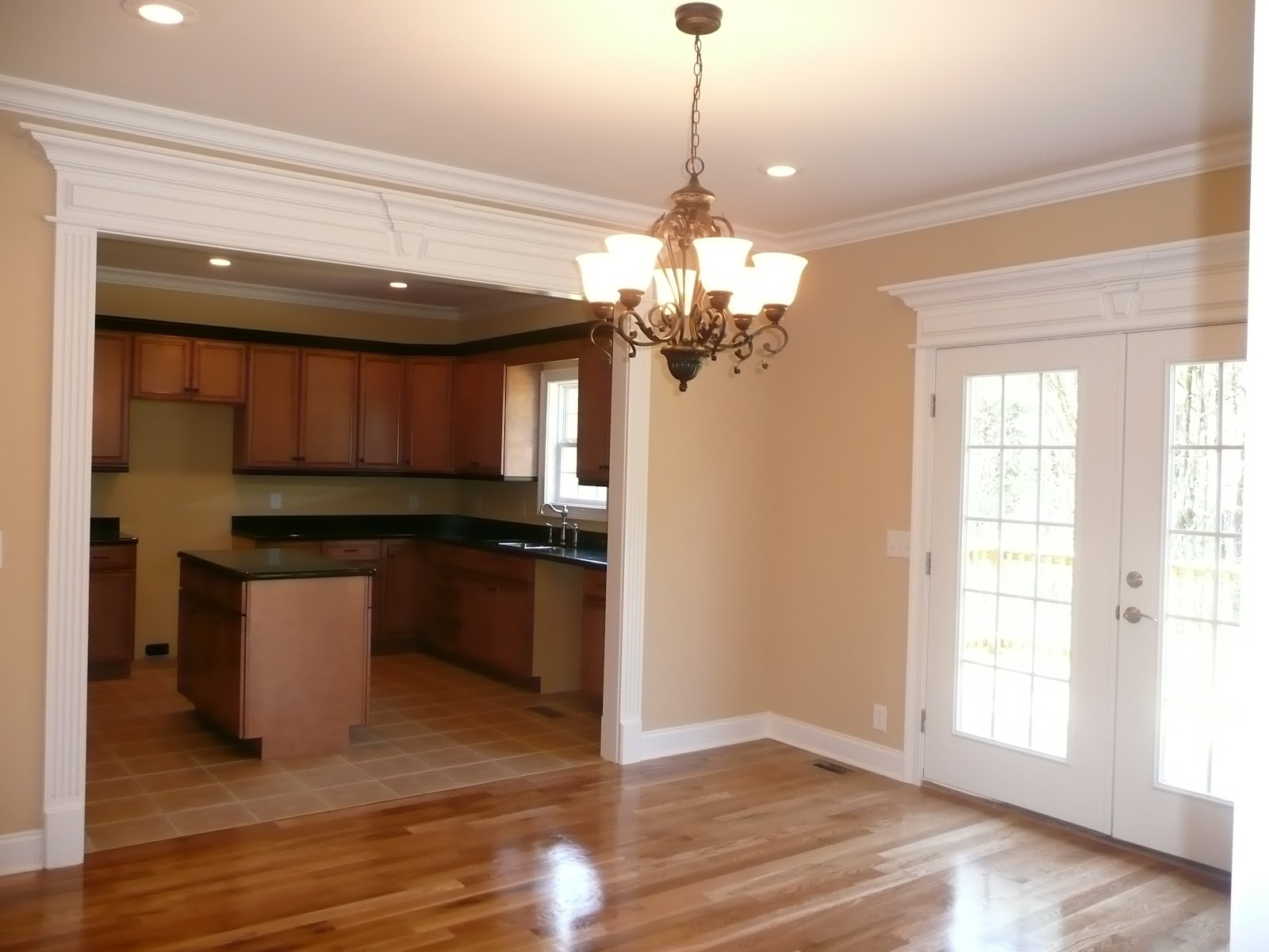 Interior view from a room with hardwood floors and a chandelier looking into a kitchen with dark wood cabinets and a center island.