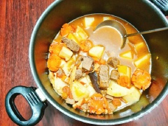 Đặt nồi lên bếp cùng với 2 muỗng canh dầu ăn, khi dầu nóng thì cho tỏi băm còn lại vào phi cho thơm. Sau đó, cho cà chua vào xào tới khi cà chua chín mềm mới đổ bát thịt bò đã ướp gia vị vào xào chung. Thêm tương cà và đổ nước sôi xâm xấp mặt thịt rồi hầm cho thịt bò chín mềm, cho khoai tây, cà rốt vào hầm thêm 10-15 phút nữa, nêm 2 muỗng cà phê hạt nêm, 1 muỗng cà phê bột ngọt cho vừa miệng là tắt bếp.