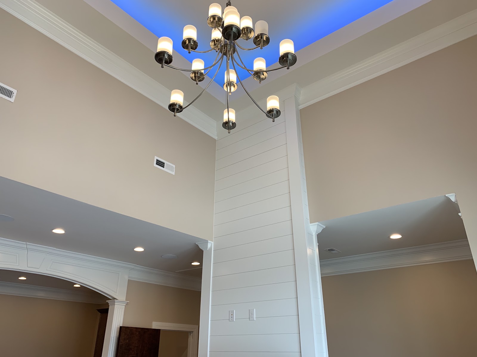 A multi-bulb chandelier hanging from a high ceiling with a blue-lit recessed section in a health clinic.