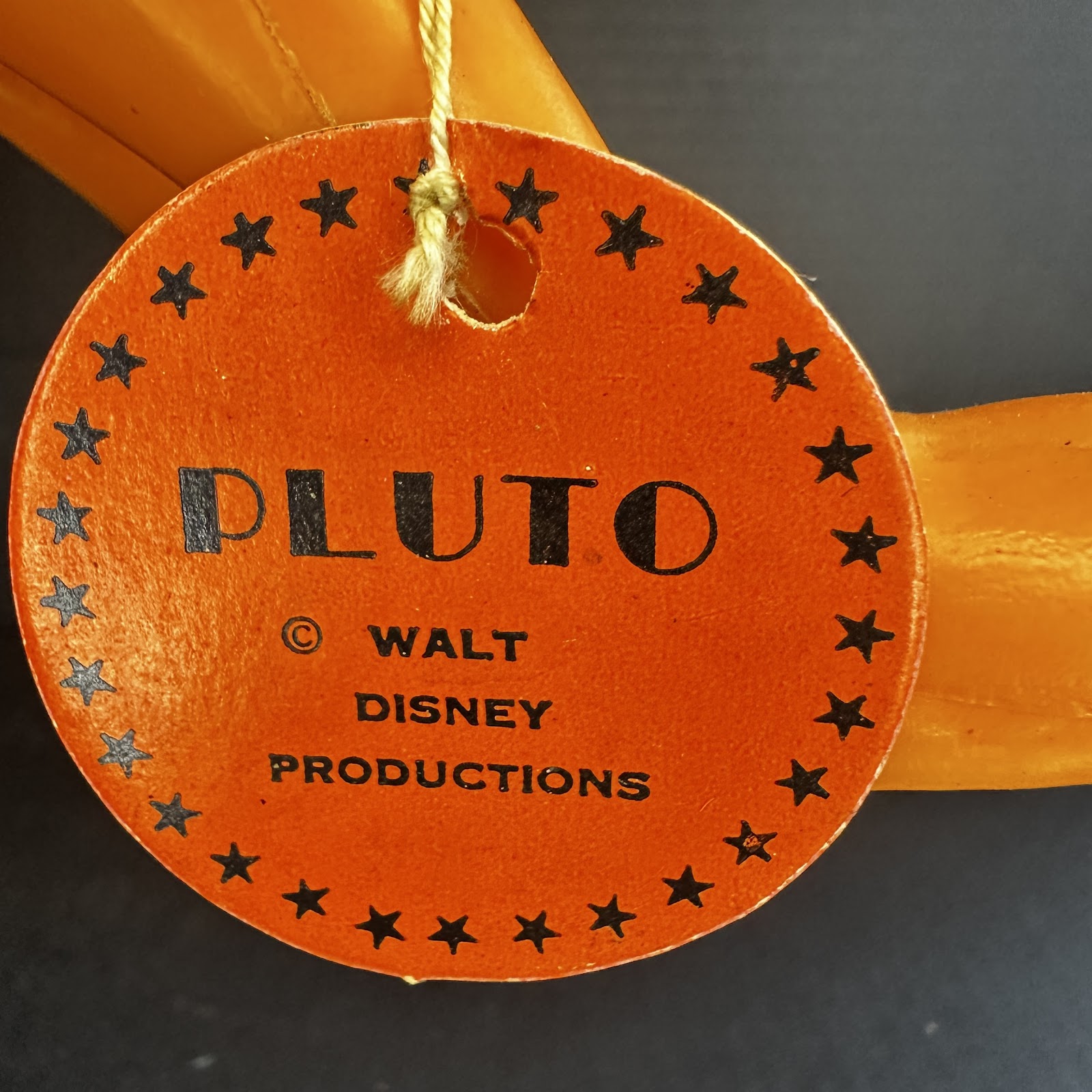 Vintage round orange cardstock hang tag reading "PLUTO" and "© Walt Disney Productions" with star border and cotton string, showing age-appropriate wear