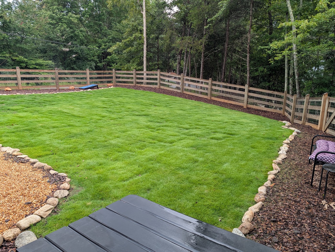 Fenced yard with fresh green lawn, stone-lined fire pit area, and yard games at Orchard & Vine Mountain Haus in Ellijay, Georgia