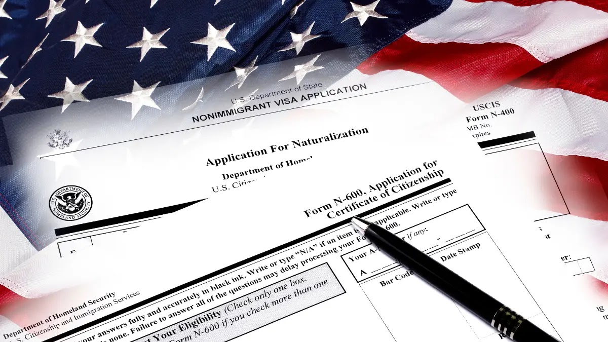 Formulários do USCIS — N-400, N-600, Application for Naturalization — sobre bandeira americana, com caneta