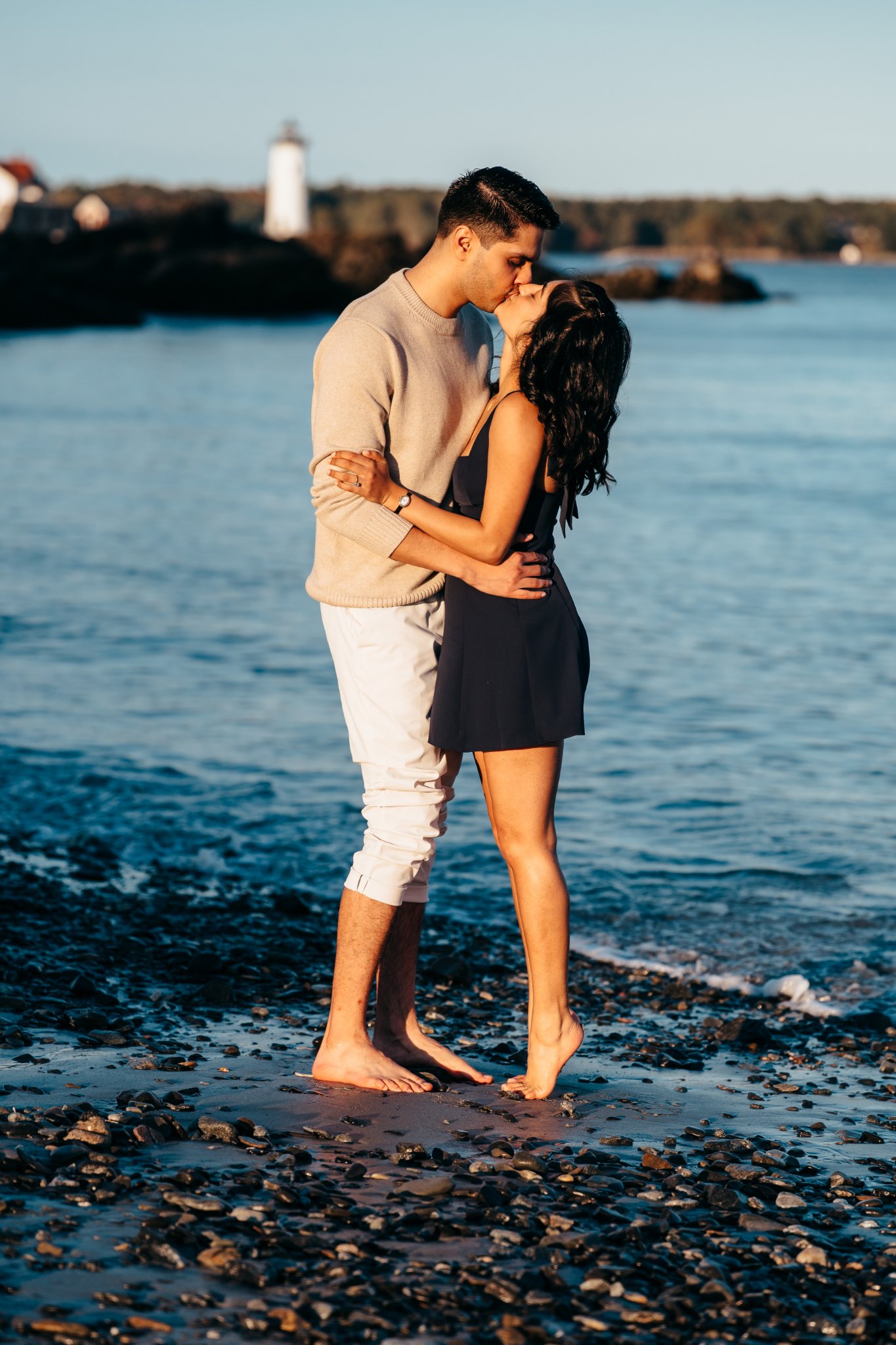 Sumeet and Jasmine kissing on the pebbly beach at the water's edge