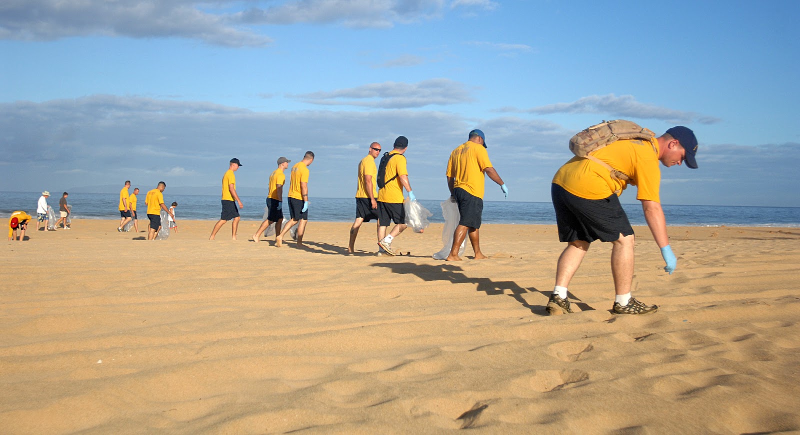US Navy Personnels in yellow shirts walking along sandy beach to pick up litters during World Ocean Day