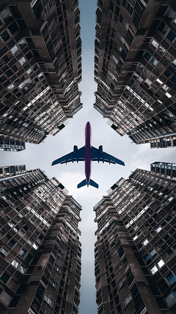 Airplane Flying Between Towering Skyscrapers from Below - Free mobile Wallpaper