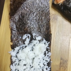 Thêm tương ớt vào phần cá hồi mayo, trộn đều. Nêm cơm với dấm sushi cho vừa miệng. Miếng rong biển cắt làm đôi. Đặt cơm lên 1 phía của miếng rong biển, sau đó cuộn lại theo chiều xéo. Dùng muỗng xúc cá hồi mayo vào bên trong, cuối cùng xếp cá hồi cắt hạt lựu lên bên trên.