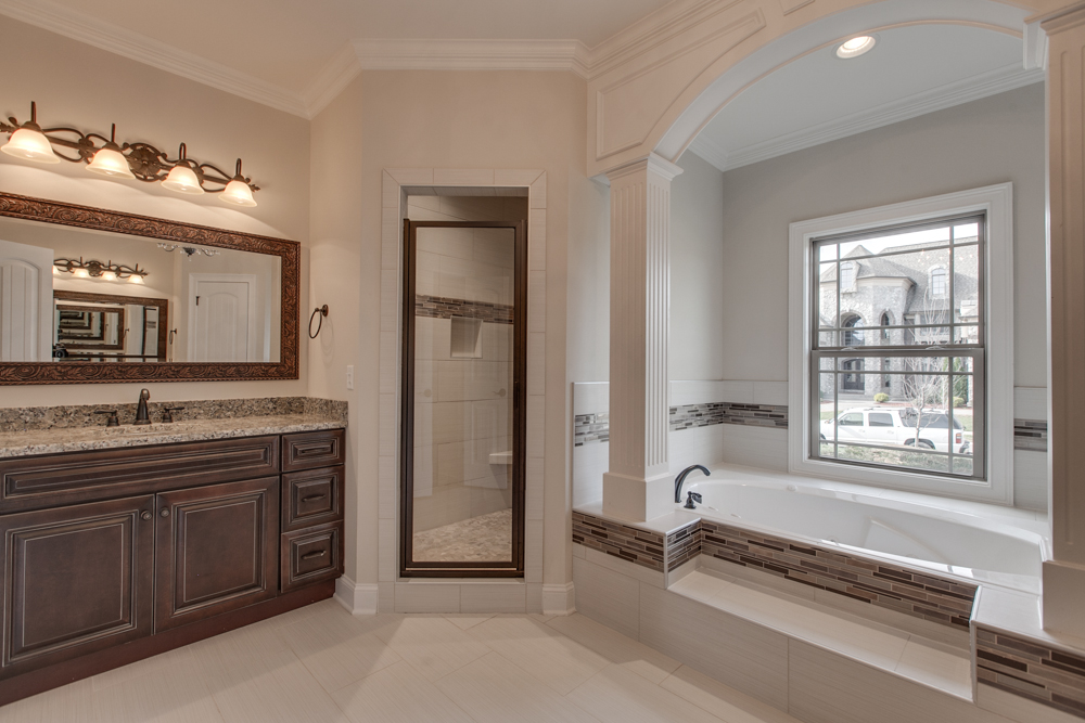 Bathroom interior featuring a dark wood double vanity with granite countertops, a large framed mirror, and a built-in bathtub with decorative tile surround.