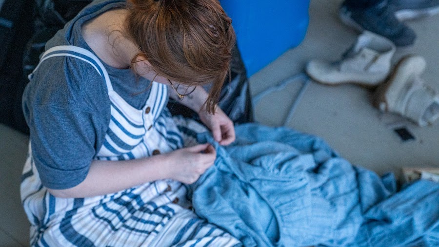 A costumer mends a blue dress on the floor