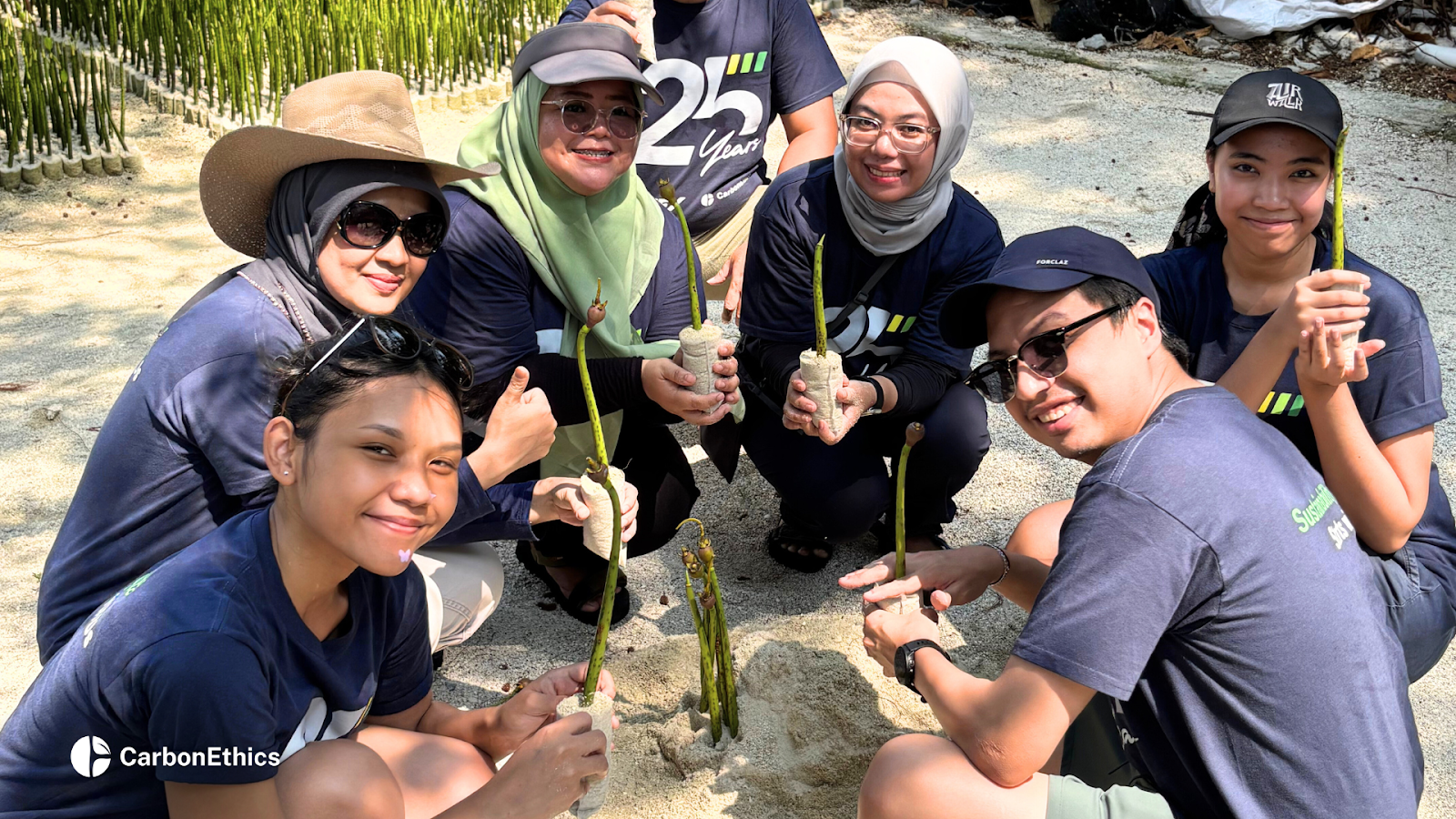 Group of MIFX team members holding mangrove seedlings while gathered on sandy ground at the nursery during a collaborative planting activity.