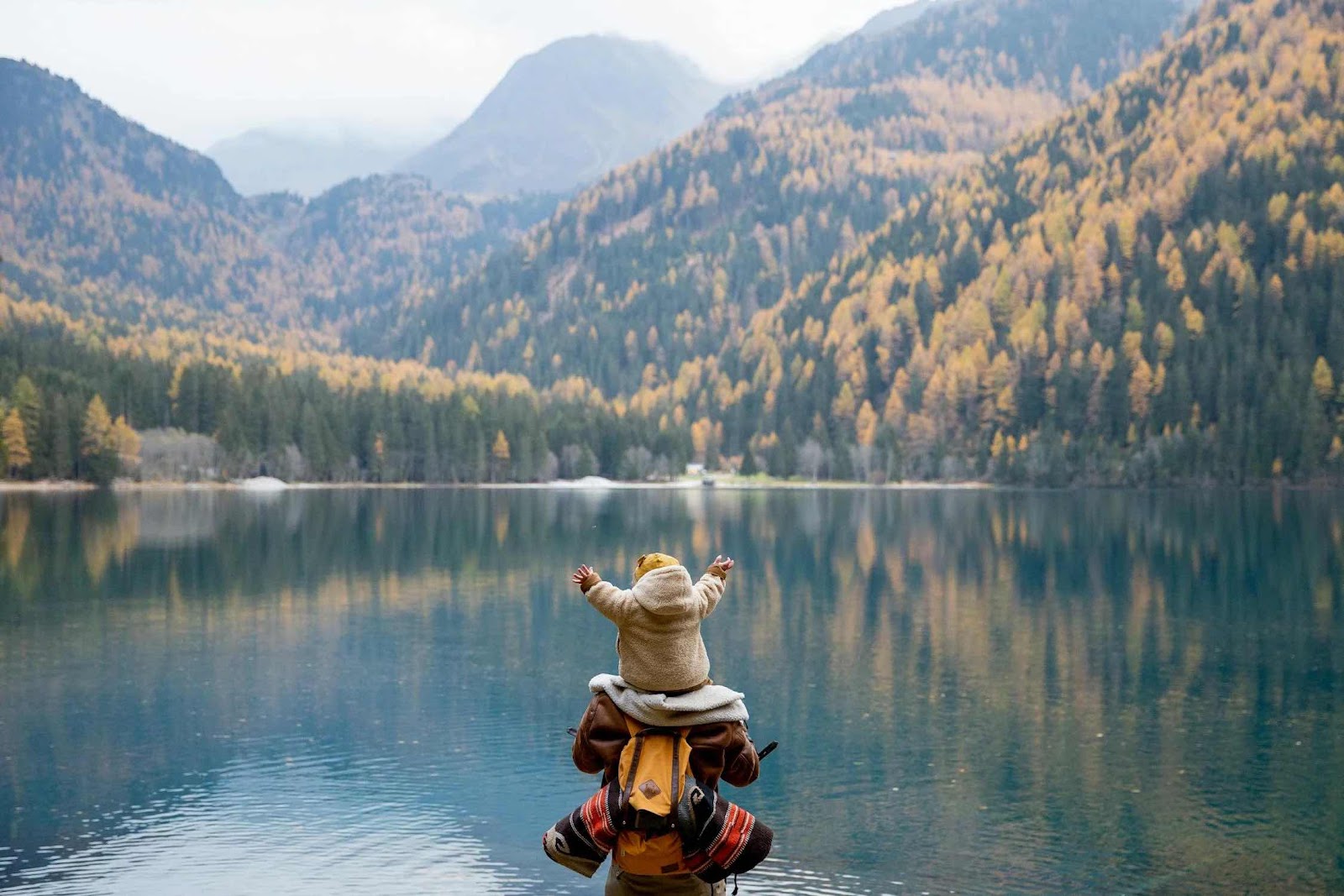 A person carrying a baby and looking at the lake.