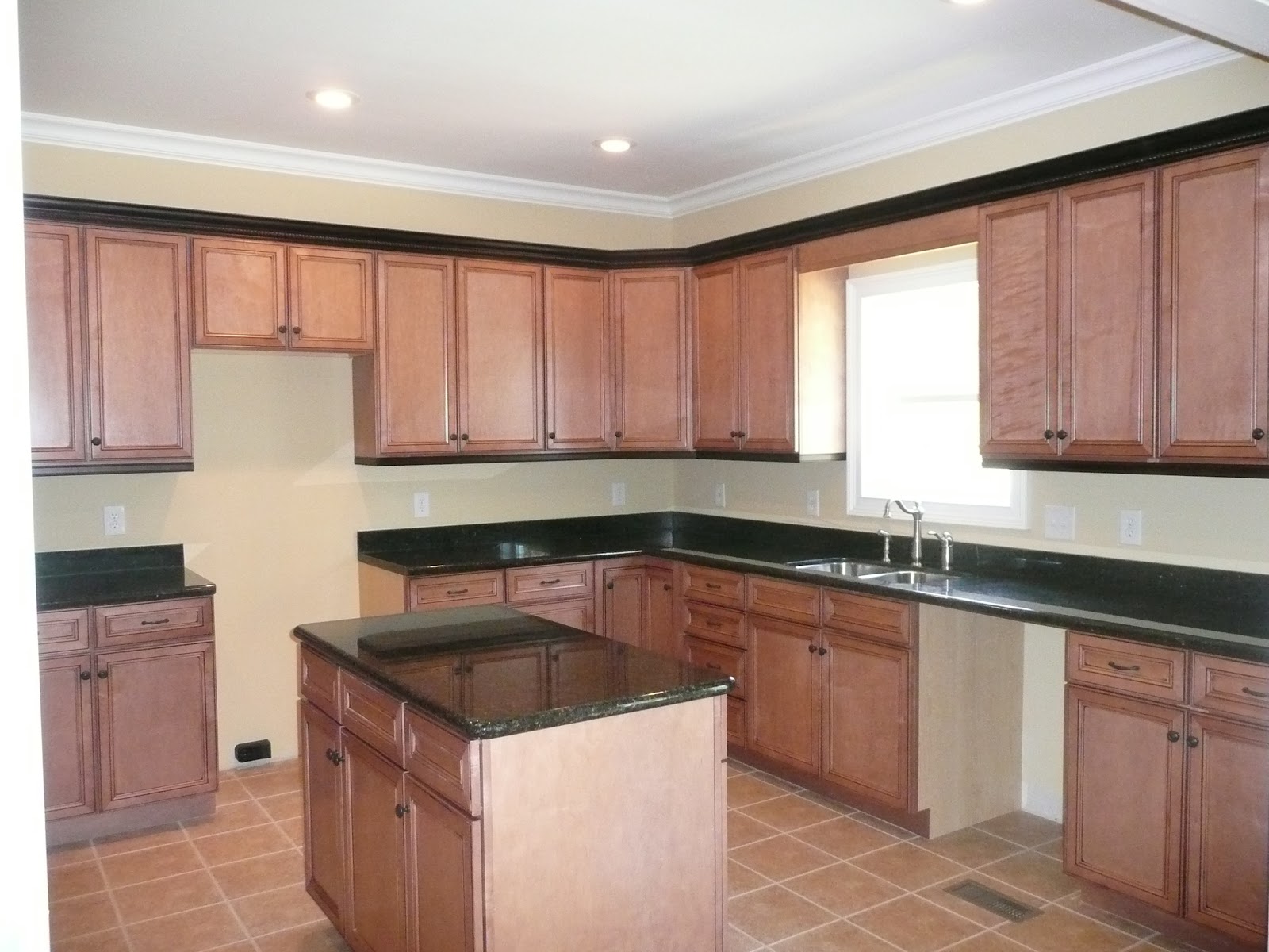 Kitchen featuring wood cabinets, black countertops, a central island, and tile flooring.