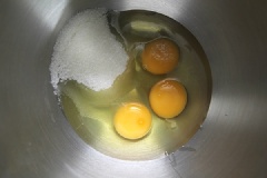 Phần cốt bánh: Vặn lò ở 180 độ, lót giấy nướng vào khuôn. Trộn đều bột hạnh nhân và bột mì. Hòa sữa tươi, dầu ăn và tinh chất vani với nhau. Cho trứng và 75gr đường vào âu lớn, đánh trứng đến khi được hỗn hợp bông đặc và không còn bọt khí nữa là được (10-15 phút).