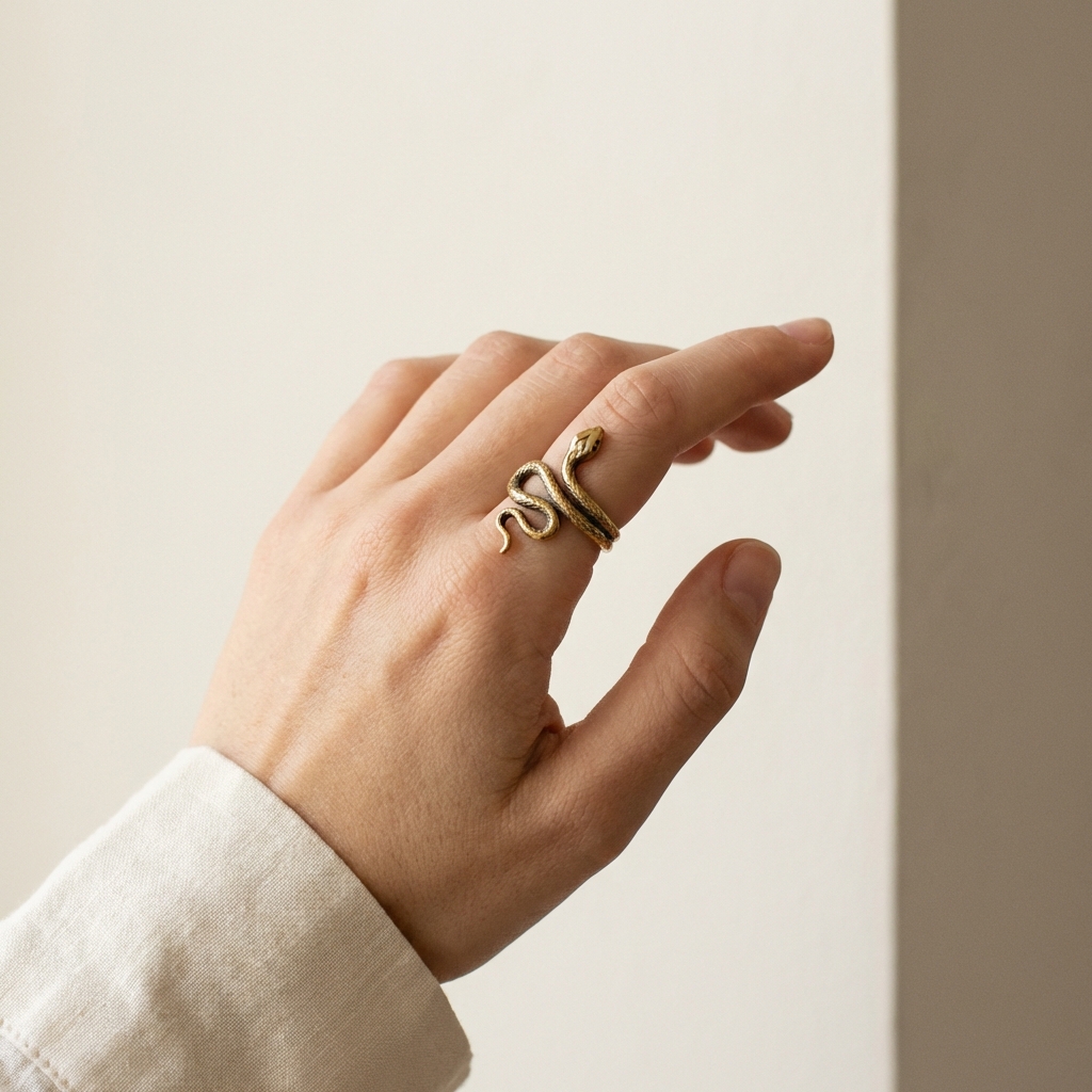 Curator style full frame close up of an ouroboros snake ring on an index finger against a minimal Aurora Antiqua background #ede7da with warm gold accents