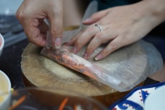 Tiếp đến là bước cuốn chả giò. Chuẩn bị 1 chén nước để làm ướt bánh tráng. Đặt bánh tráng đã được làm mềm lên một tấm thớt, cho nhân vào vị trí 1/3 bánh tráng, gấp 2 bên mép và cuốn chặt tay để chả giò không bị bể.