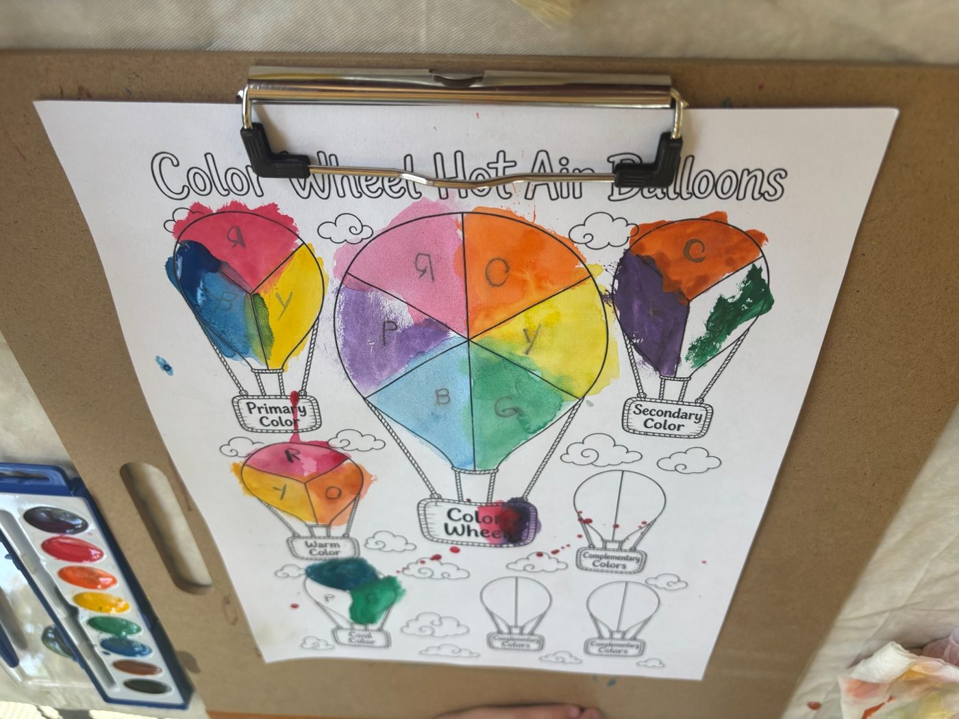 A completed color wheel hot air balloon worksheet on a clipboard