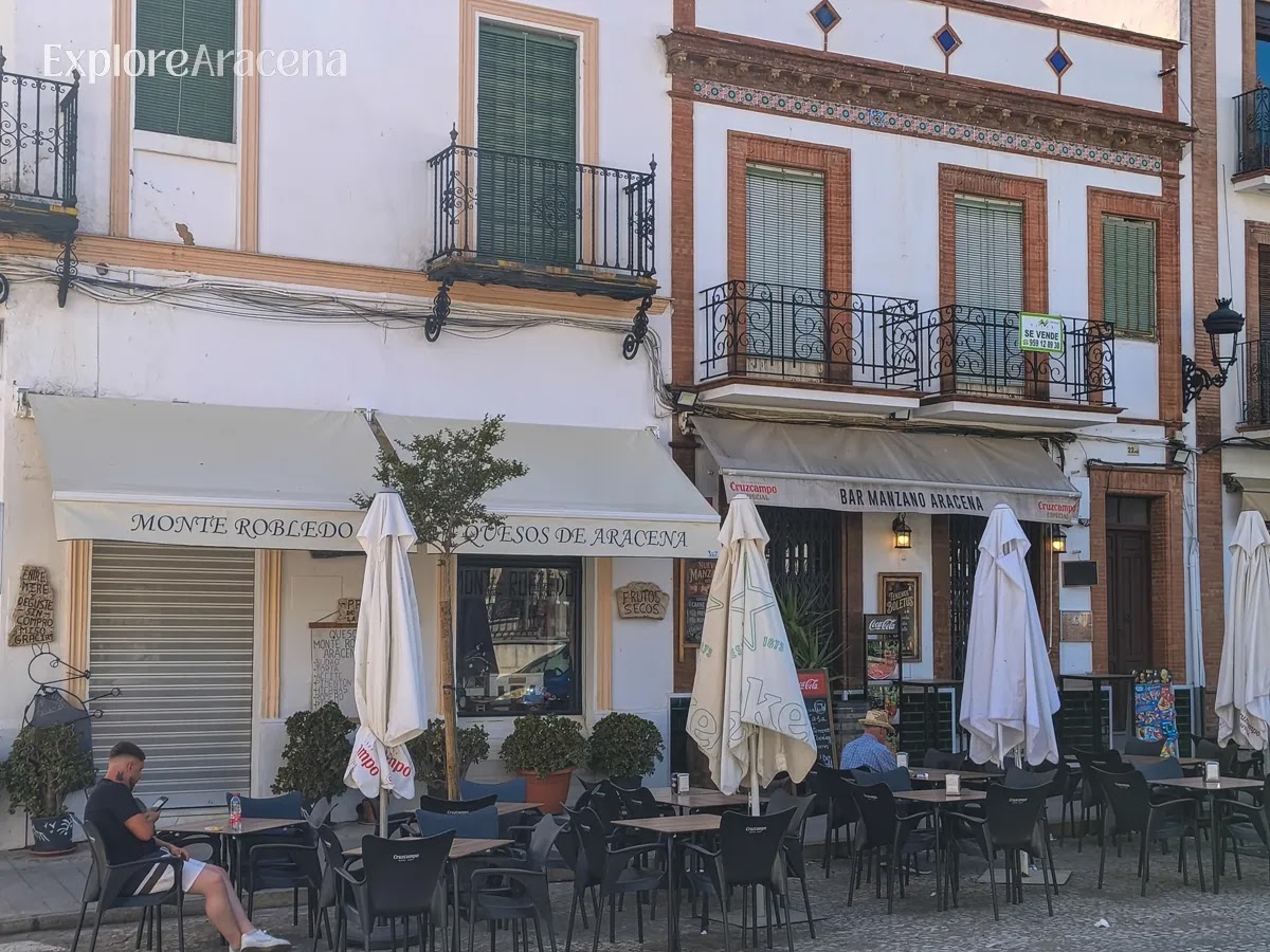 People relaxing on a bar patio in Aracena with plates of Monte Robledo cheese and local food on the table at Bar Manzano.