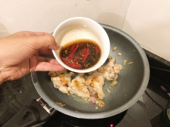 Cho phần sốt gồm 80ml dầu mè, 80ml nước tương, 80ml rượu gạo, 1 muỗng canh đường cát trắng, 1/4 muỗng canh bột nêm vị gà và 50ml nước lọc. Đảo đều sốt, đậy nắp kín rồi đun lửa nhỏ cho đến khi thịt gà thấm sốt và có màu cánh gián đẹp mắt. Sốt cũng keo sánh lại rất thơm. Sau đó cho một ít húng quế vào, xào sơ chừng 30 giây thì tắt bếp.