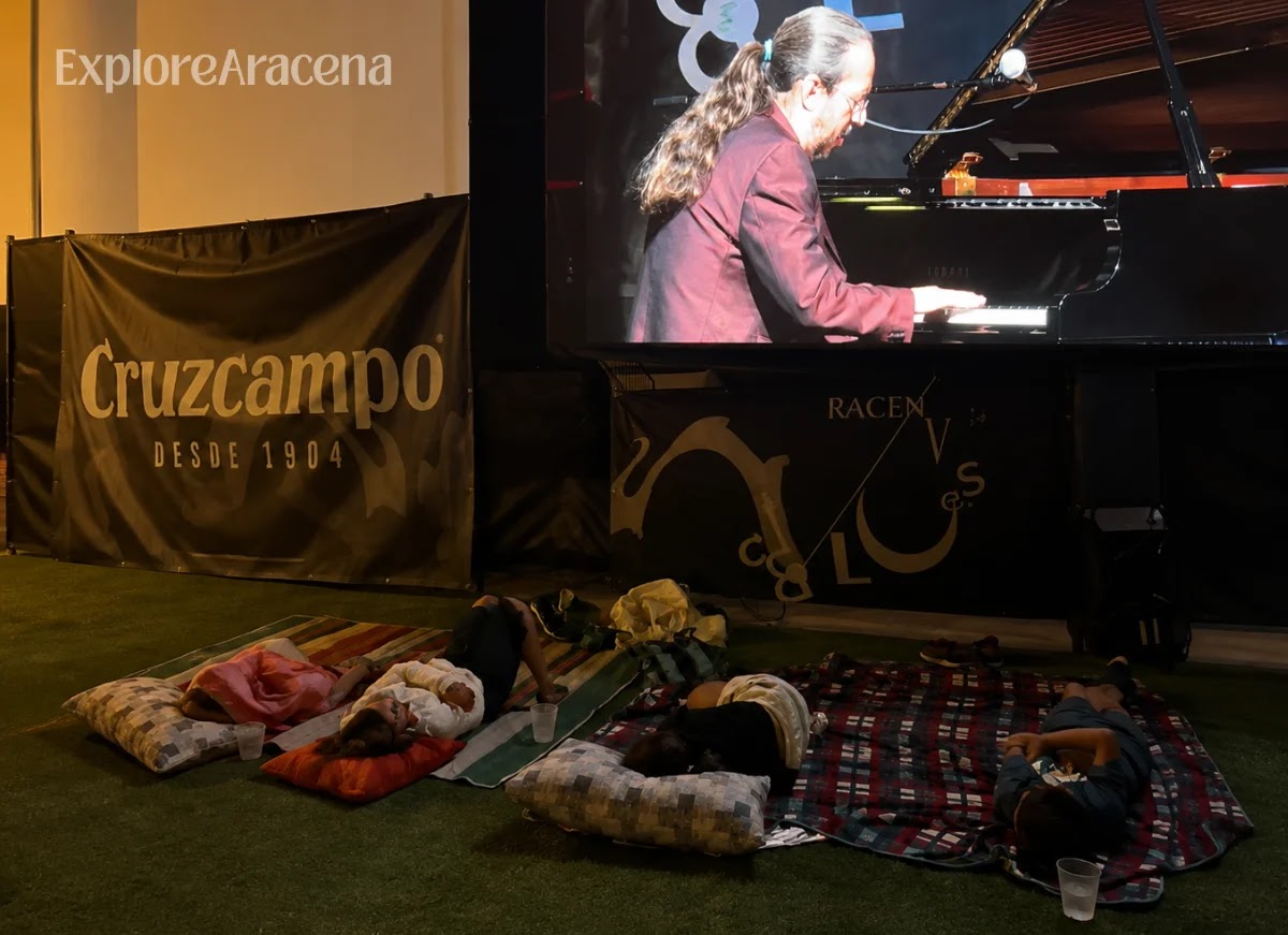 Children sleeping in sleeping bags beside the stage while the Aracena Blues concert continues nearby.