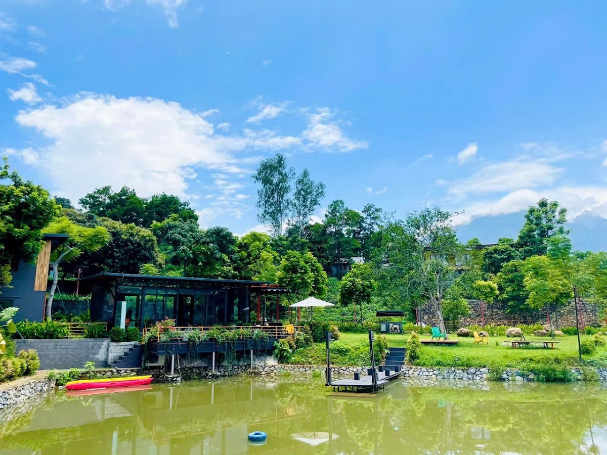 Toàn cảnh An Trà Retreat Ba Vì nhìn từ mặt hồ, nhà mái thấp dưới hàng cây