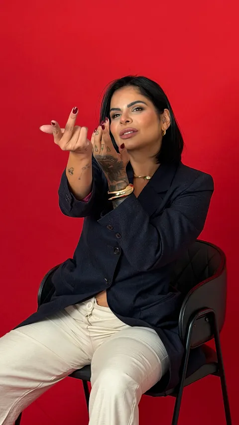 Mulher de blazer azul-marinho gesticulando, sentada em fundo vermelho
