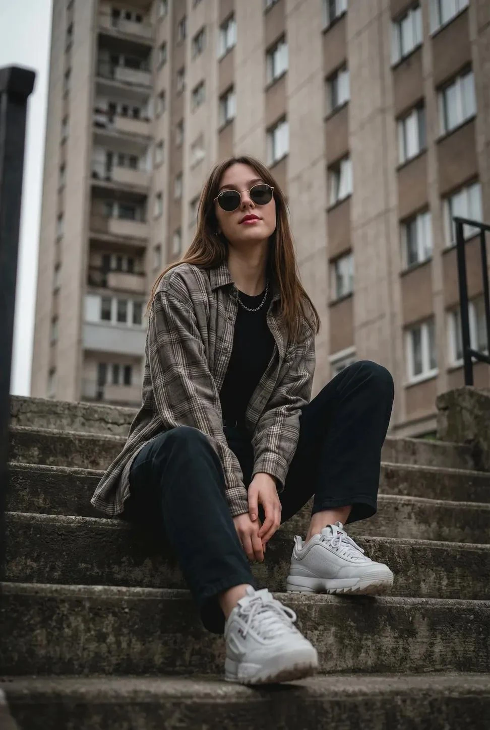 Una joven sentada despreocupadamente en unas escaleras de cemento al aire libre, posando con una actitud serena y segura.