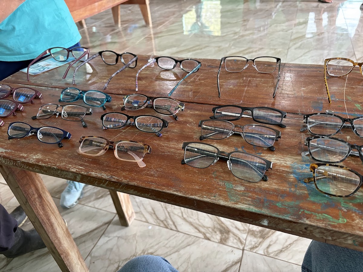 Dozens of pairs of donated reading glasses laid out in rows on a wooden table at the Belize clinic, June 2026