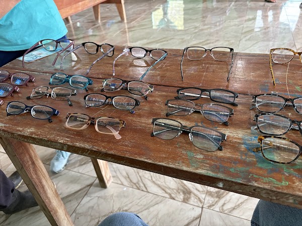 Dozens of pairs of donated reading glasses laid out in rows on a wooden table at the Belize clinic, June 2026