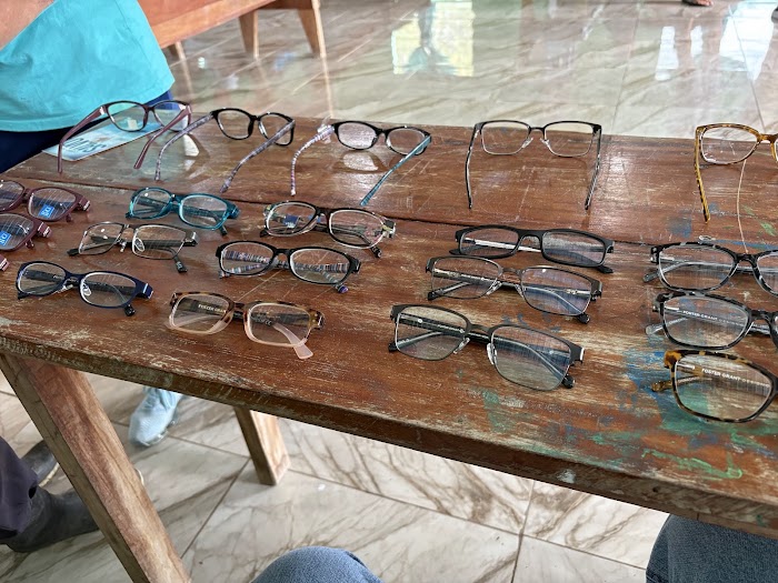 Dozens of pairs of donated reading glasses laid out in rows on a wooden table at the Belize clinic, June 2026