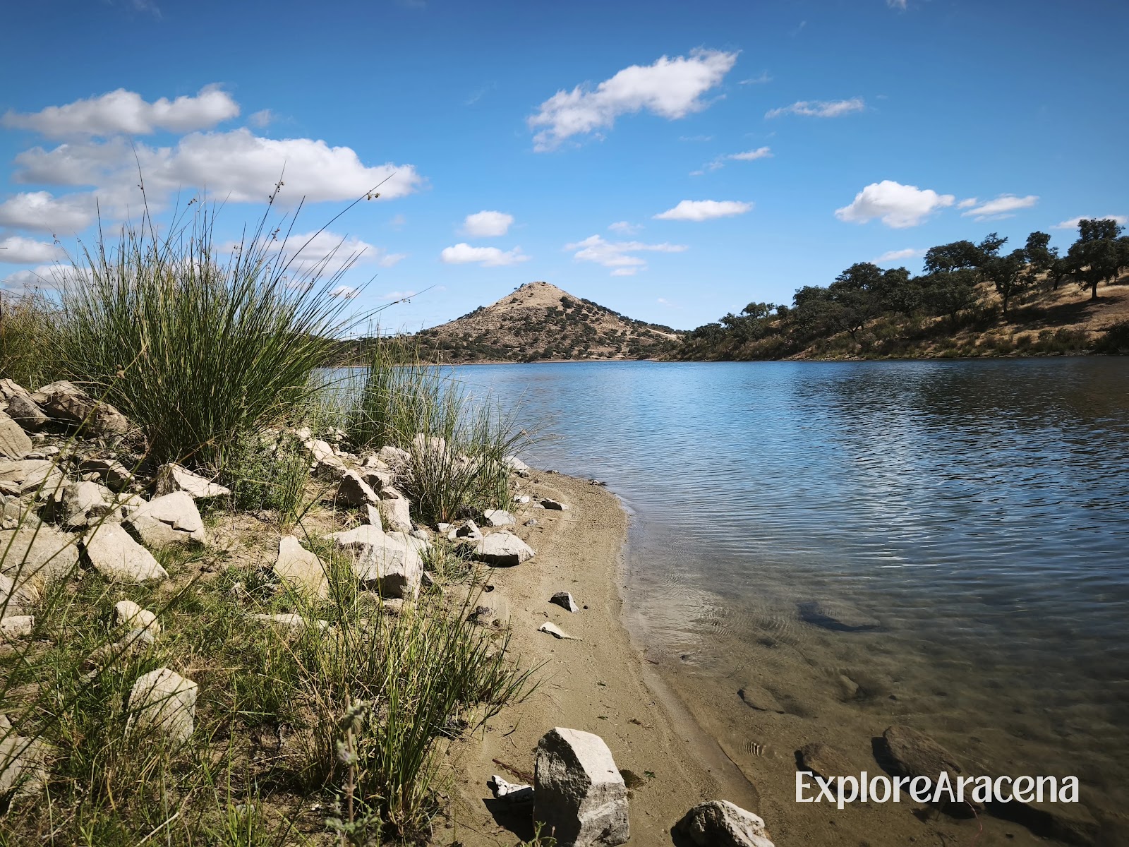 View from the shoreline of a reservoir surrounded by hills in the Sierra de Aracena.