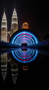 Dramatic Night Reflection of Petronas Towers and Light-Painted Blue Tunnel in Wet Foreground