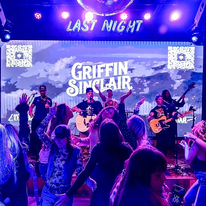 Servers navigating through crowded floors at This Bar carrying food and drinks while live music plays in the background