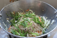 Vẫn sử dụng chiếc chảo ấy, cho thêm 1 muỗng canh dầu ăn rồi trút rau vào xào trong 5 phút. Trút toàn bộ bún khô vào xào chung, nêm lại gia vị cho vừa ăn. Bún chín cho thịt, tôm, trứng vào trộn đều. Tắt bếp.
