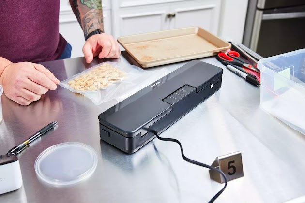 Mani sul bancone vicino alla macchina sottovuoto Anova Precision Sous Vide e al sacchetto sigillato di cereali