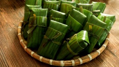 Chuẩn bị sẵn lá chuối, đặt 2 lá chuối to bên ngoài và 1 lá chuối nhỏ phía trong. Phết lên lá chuối nhỏ 1 lớp dầu ăn mỏng sau đó múc 1 phần vừa phải hỗn hợp khoai mì lên trên. Dàn mỏng khoai mì rồi đặt quả chuối vào chính giữa, quấn lá chuối nhỏ lại cho khoai mì bao bọc đều quanh quả chuối sau đó gói lại. Tước lá chuối thành những dây chuối dài để cột bánh cho cố định, làm lần lượt cho đến hết khoai mì và chuối.