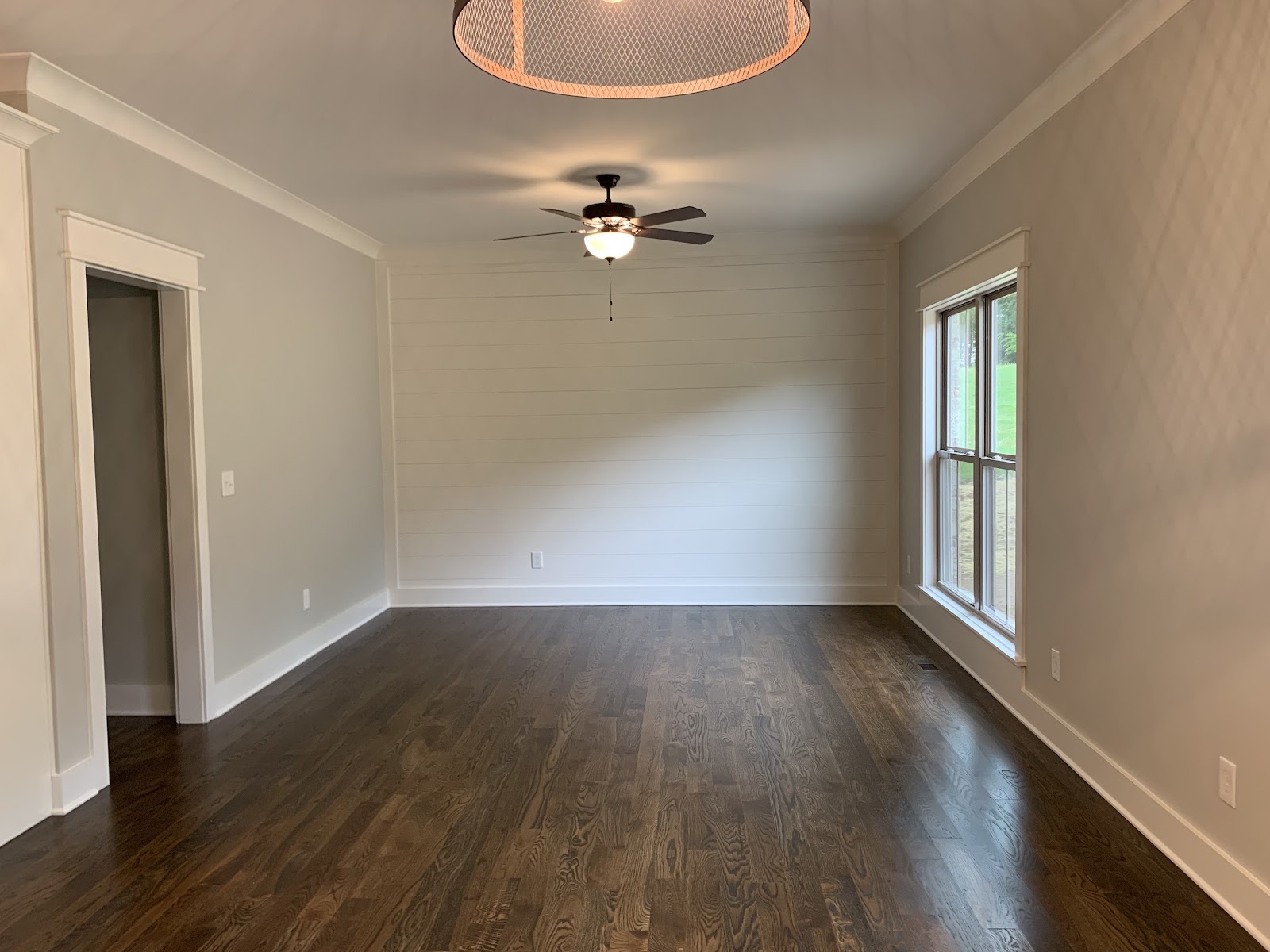 Empty room with dark wood flooring, light grey walls, white crown molding, a ceiling fan, and a large window.