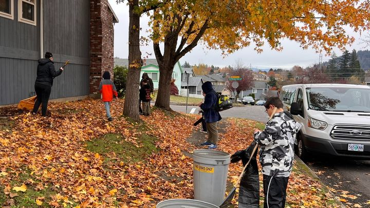 Children and adults raking a leaf-covered yard together at last year’s Leaf of Joy.