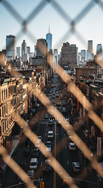 High Angle View Down a Busy Chinatown Street Towards the New York City Skyline, Framed by Wire Fence - Free mobile Wallpaper