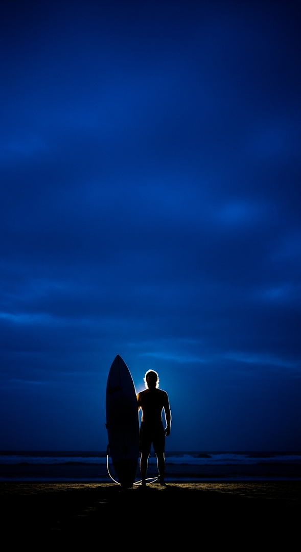Dramatic Silhouette of Surfer with Board at Night Against an Intense Blue Sky