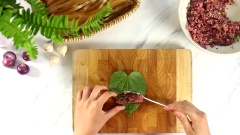 Làm chả lá lốt topping cho bánh đa cua: Cho 200gr thịt heo xay, 30gr nấm mèo băm nhuyễn vào tô cùng 10gr hành tím băm, 10gr đầu hành, 1 muỗng cà phê hạt nêm, 1/2 muỗng cà phê tiêu, 1 muỗng cà phê nước mắm rồi trộn đều. Xúc từng thìa thịt heo đã ướp vào lá lốt rồi cuộn lại.